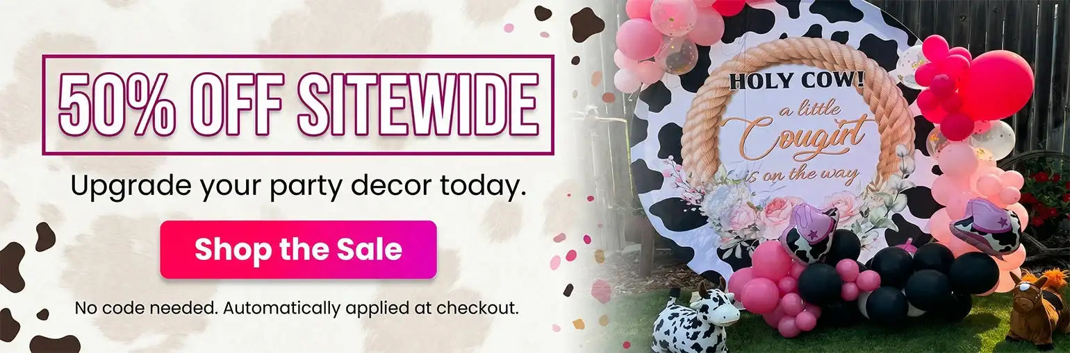 A black and white cow-themed party backdrop with a rope frame, pink and black balloons, and decorative text reading ’holy cow! A little cowgirl is on the way.’